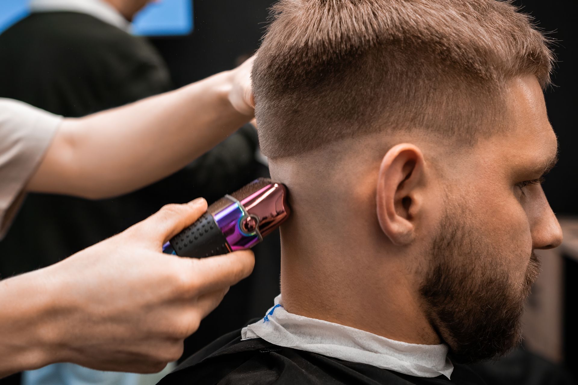 Barber using electric clippers to fade the side of a client’s haircut in a salon