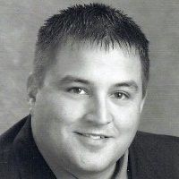 Jon Shaw in a suit and tie is smiling for the camera