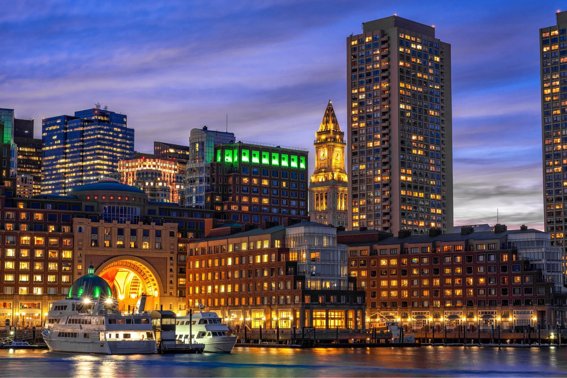 A boat is floating in the water in front of a city skyline at night.