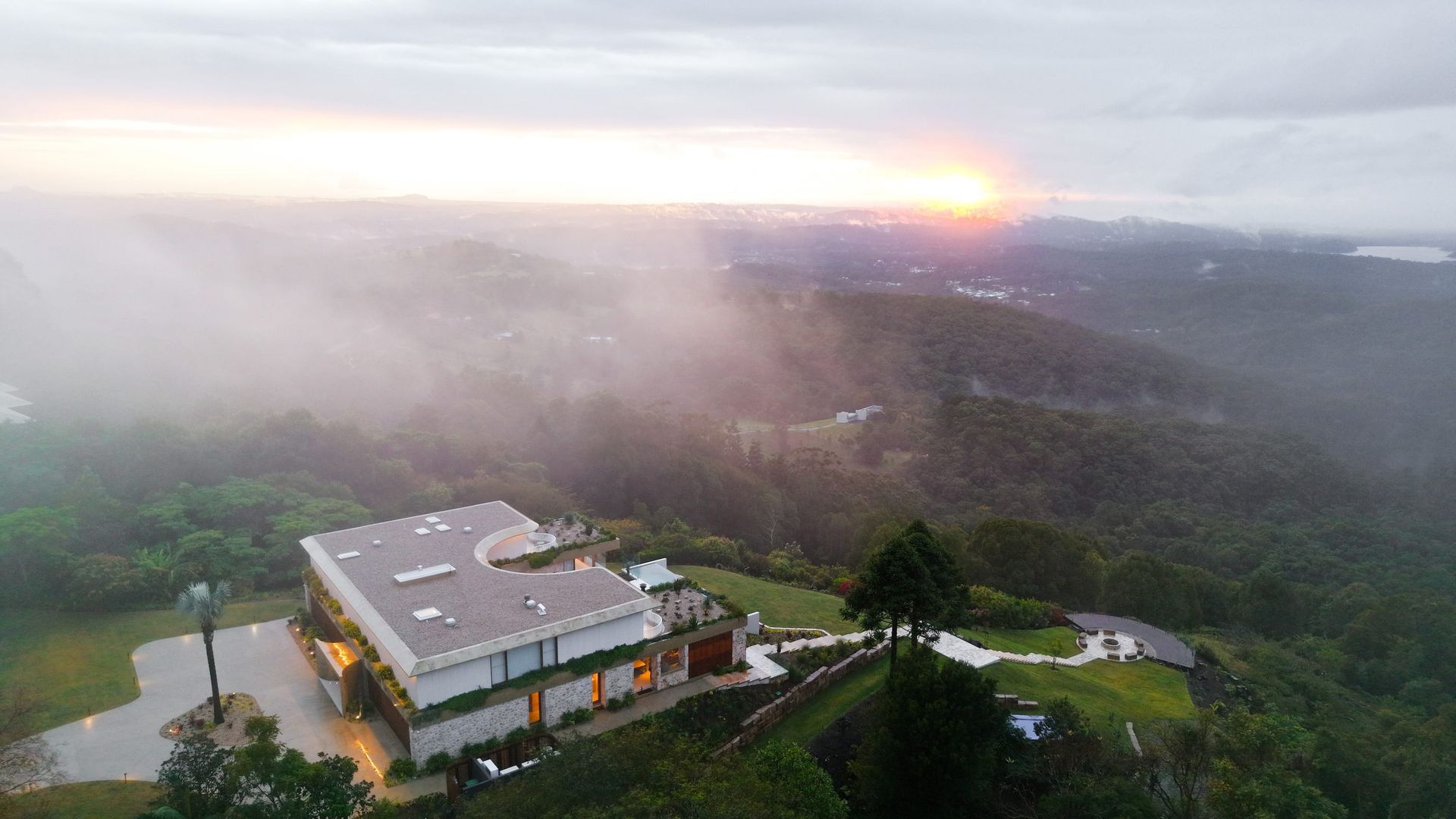 Modern house atop a hill at sunrise, partially obscured by fog.