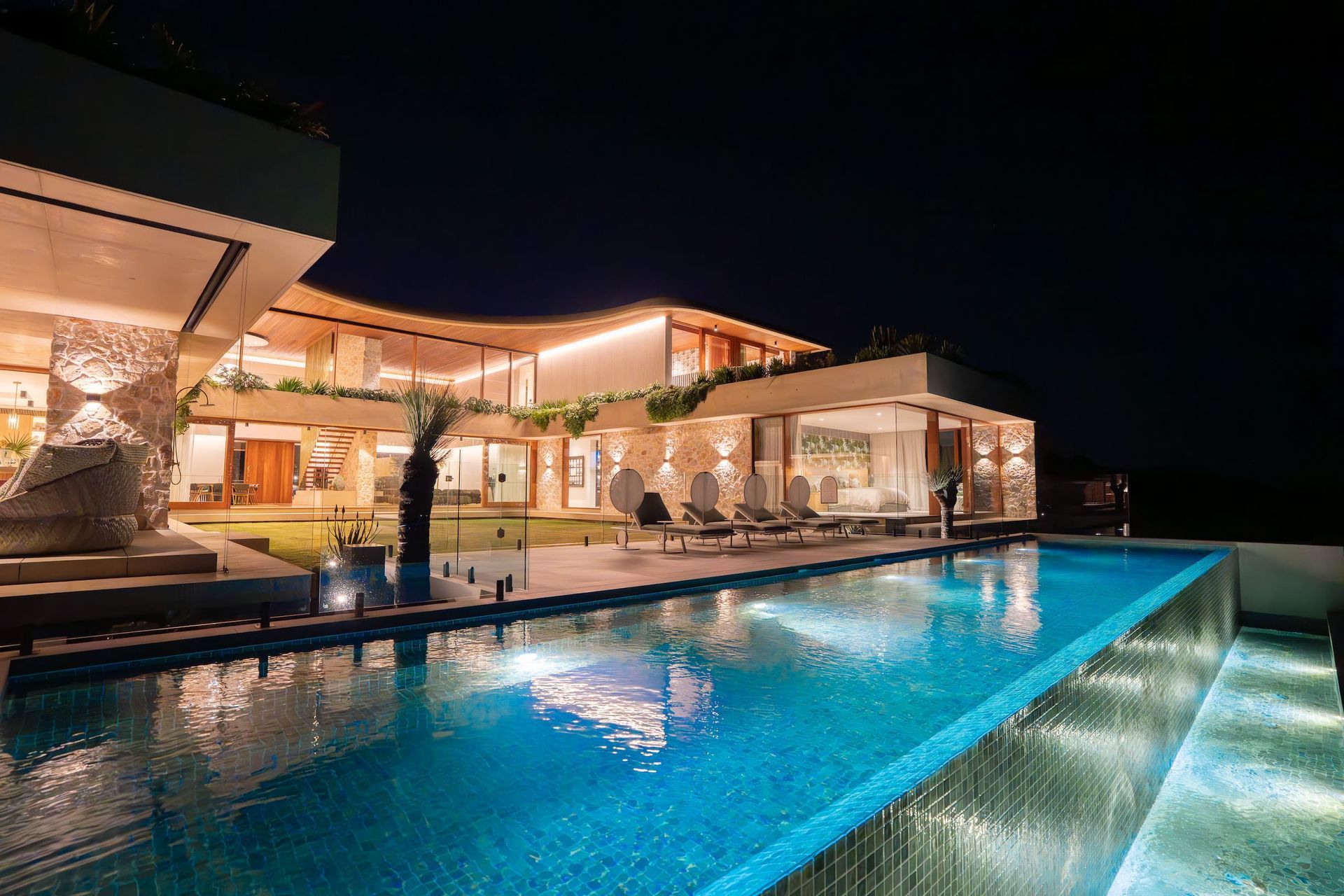 Luxury house with a long, illuminated pool at night.