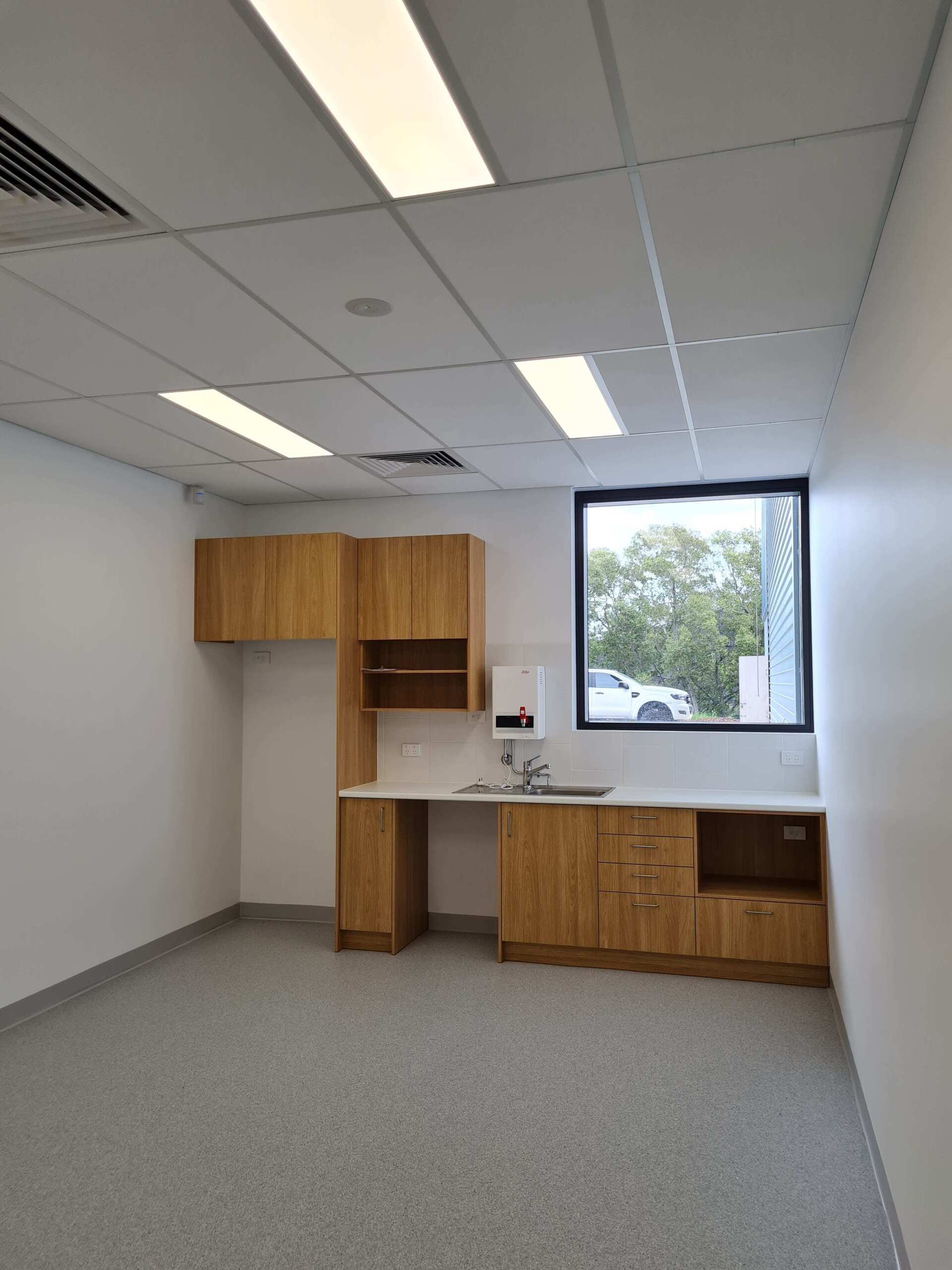 An empty room with wooden cabinets , a sink , and a window.