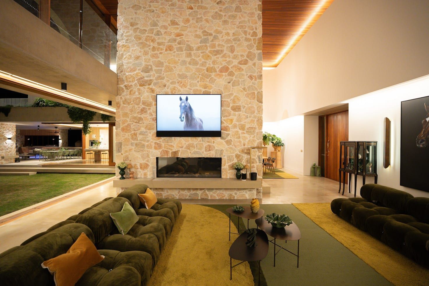 Living room with stone fireplace, TV, green sofa, and outdoor view.