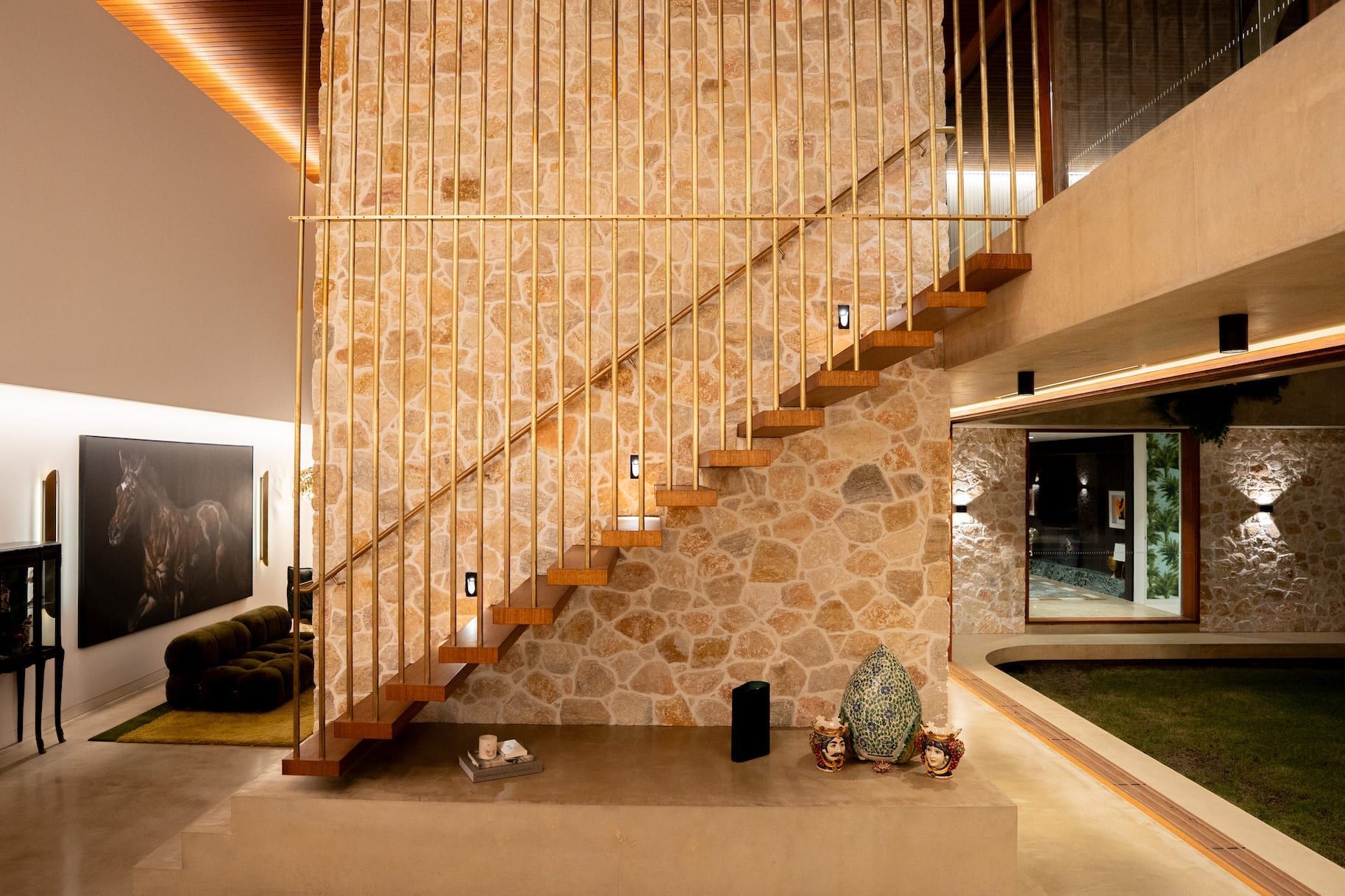 Interior with stone wall, wooden stairs, brass railings, and warm lighting.