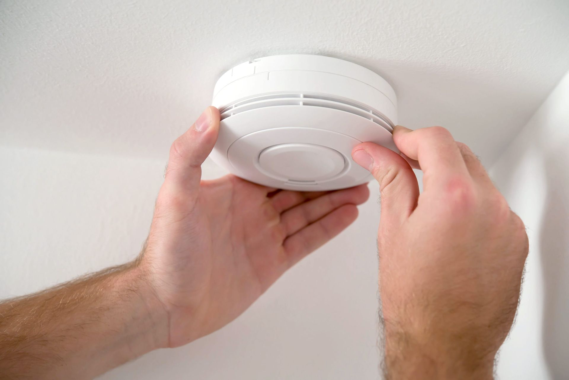 Hands installing a white smoke detector on the ceiling