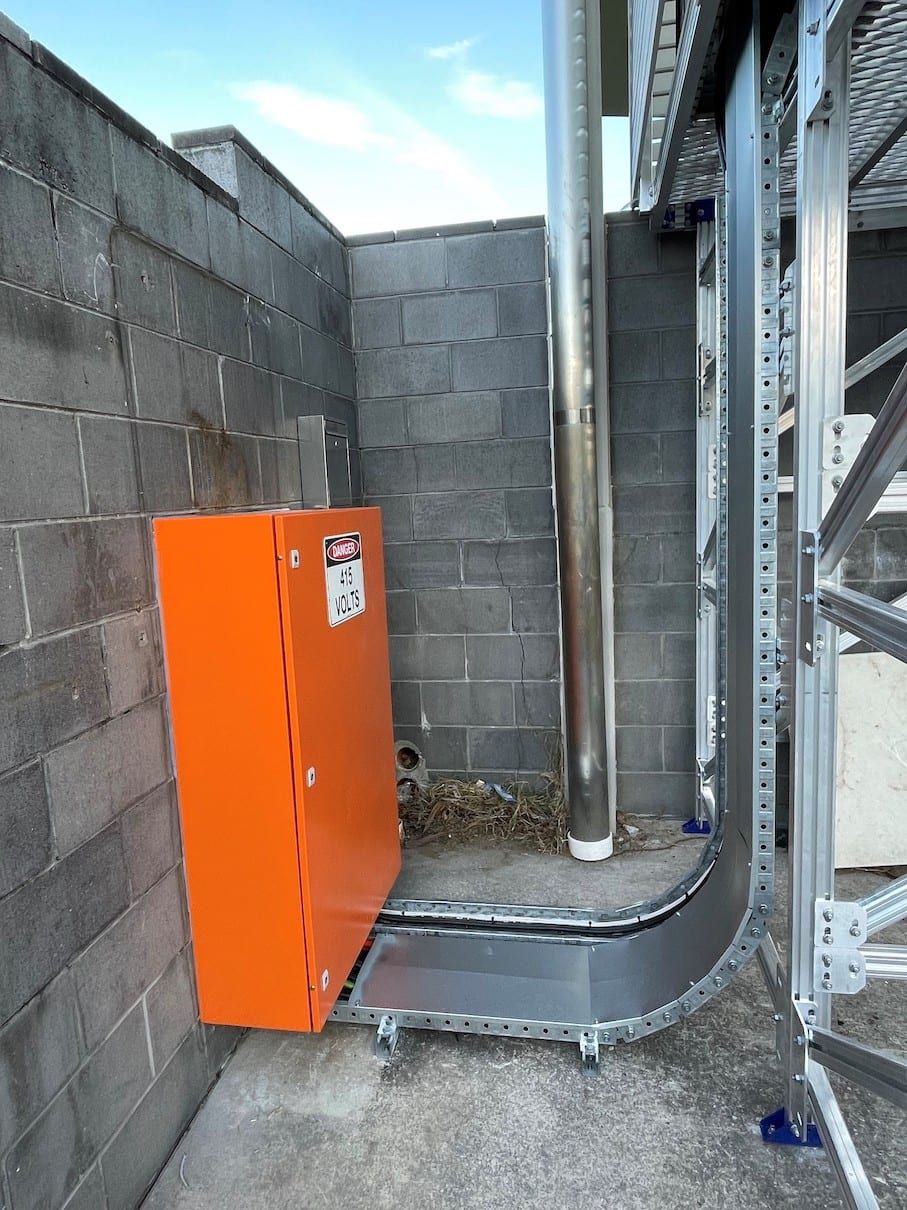 An orange box is attached to a brick wall next to a pipe.