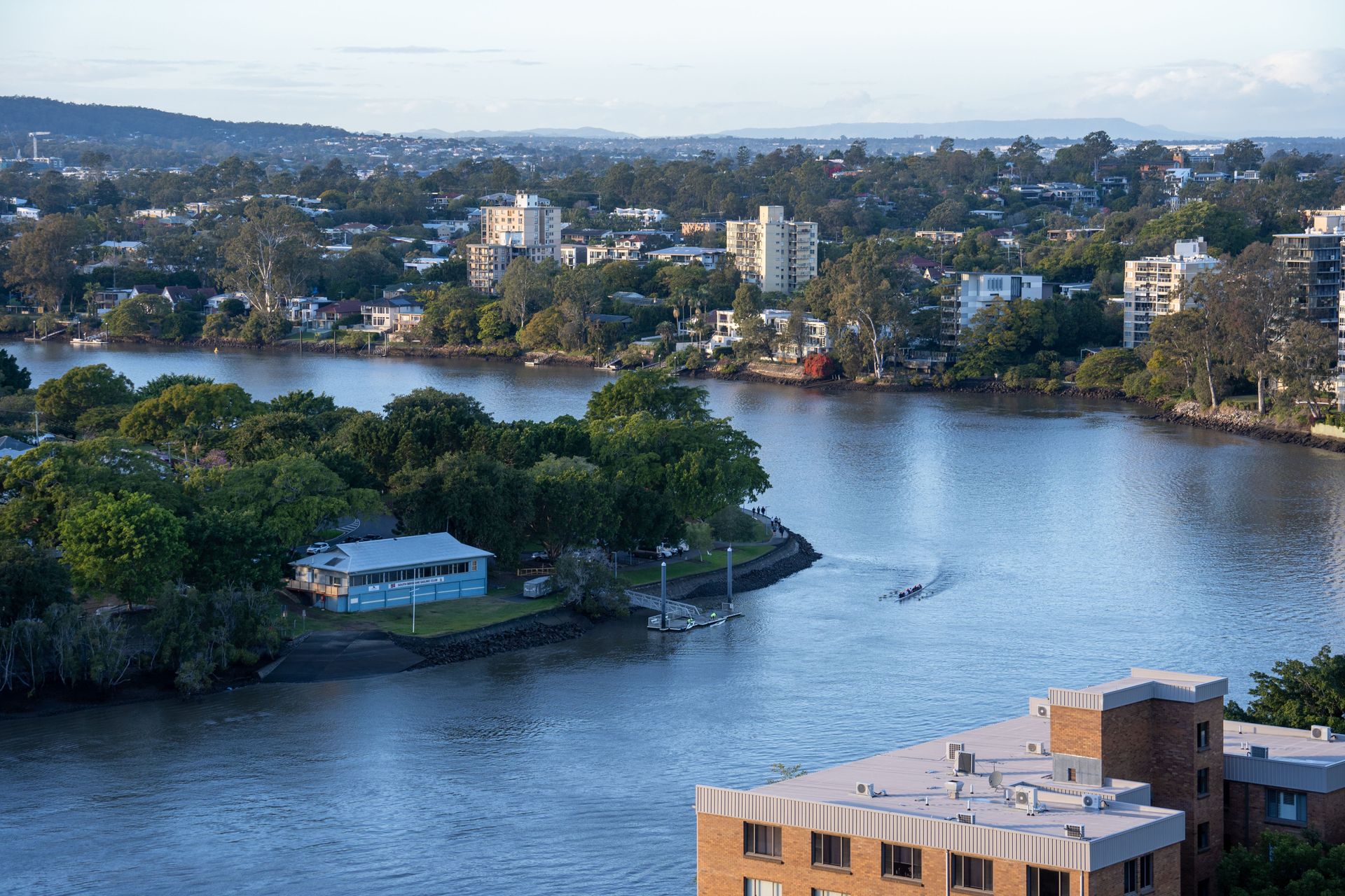 Wide river with green islands and buildings under a clear sky, viewed from an elevated city overlook
