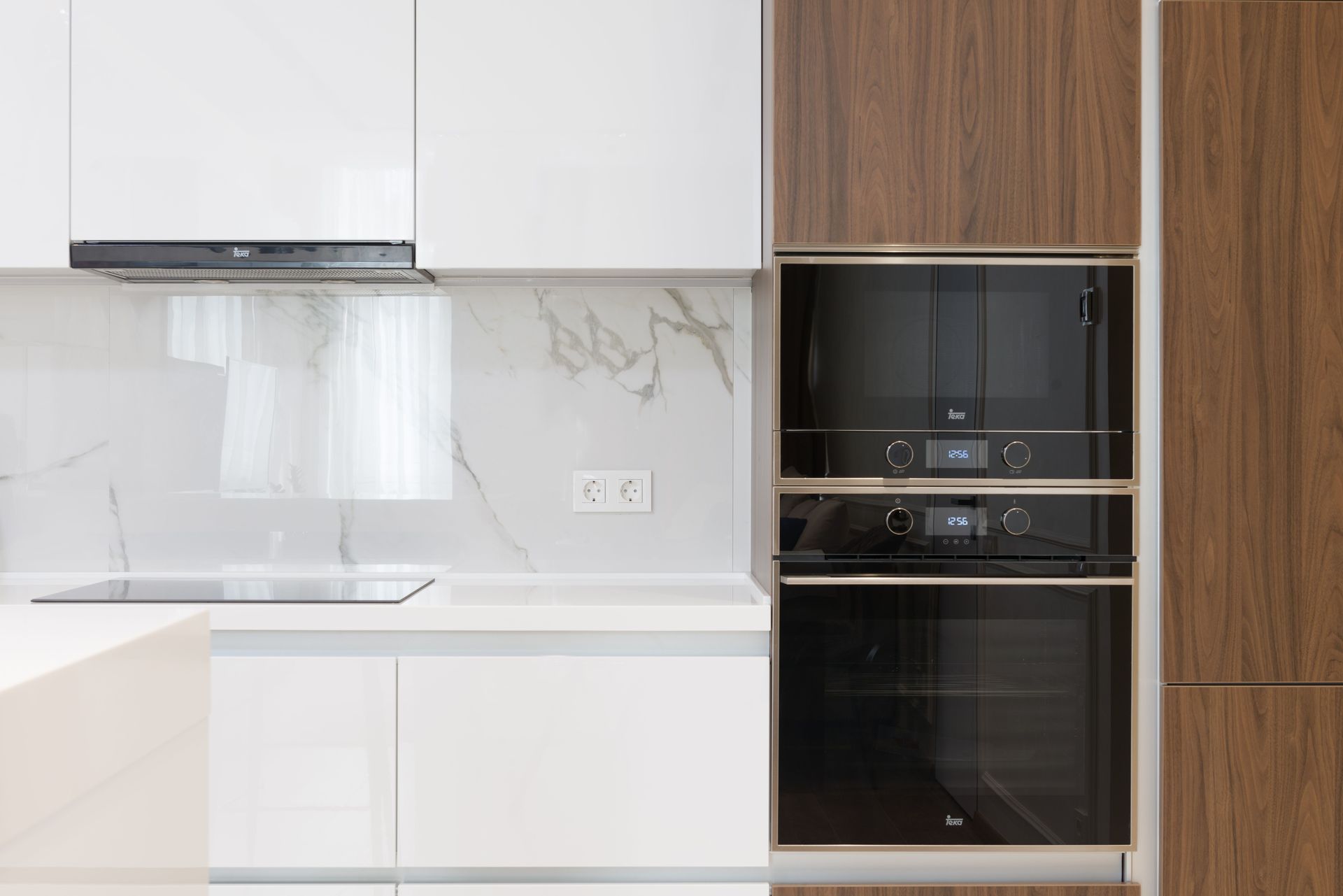 Modern white kitchen with wood cabinets, built-in black oven, and marble backsplash