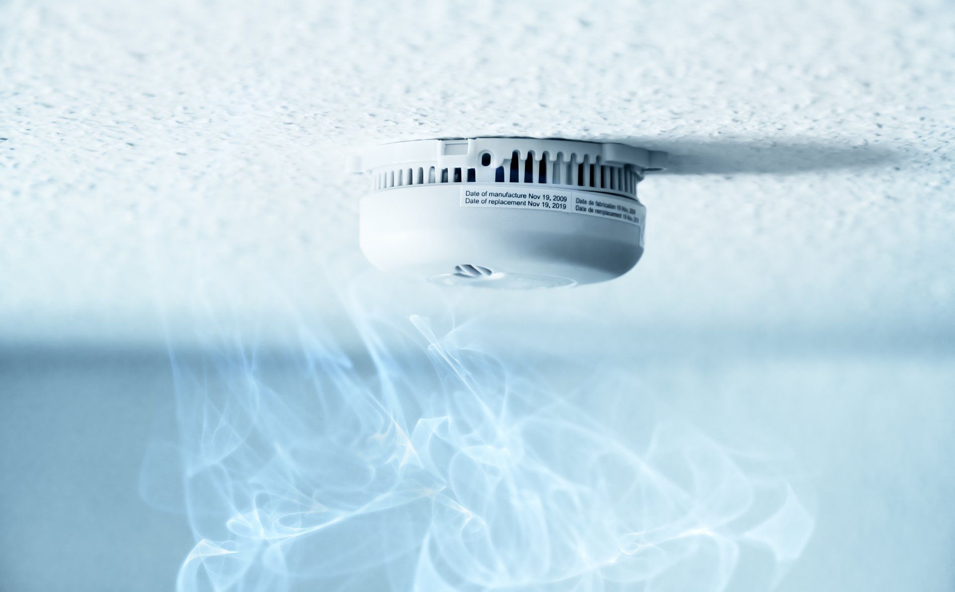 A smoke detector on the ceiling with smoke coming out of it.