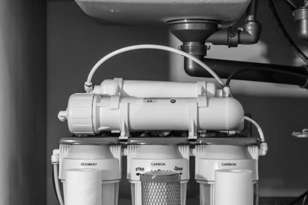 A black and white photo of a water filter under a sink.