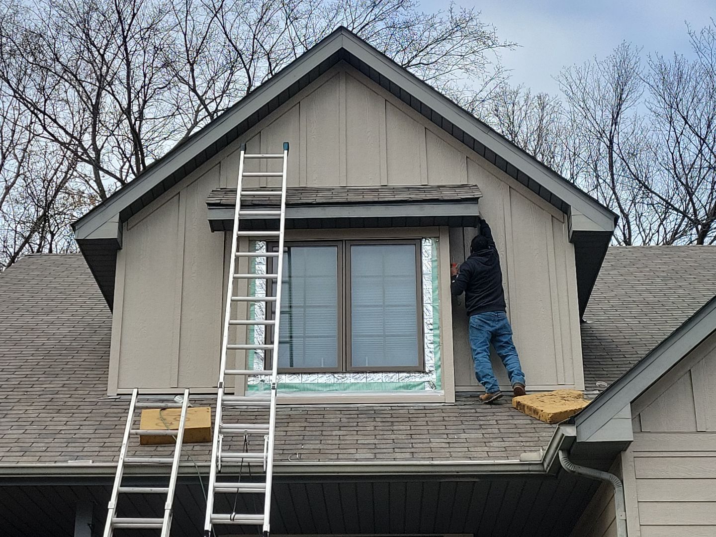 a man is working on the roof of a house with a ladder .