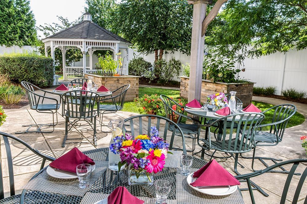 Outdoor patio dining area with tables, pink napkins, colorful flowers, and a white gazebo in the background