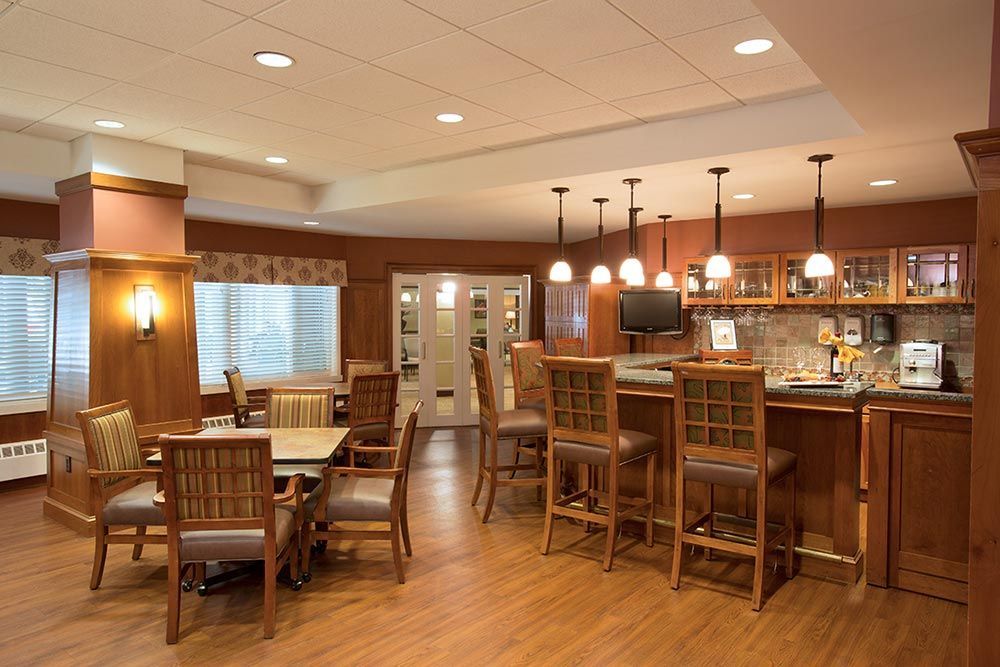 Warm wood-paneled kitchen and dining area with bar stools, pendant lights, and a dining table by a window.