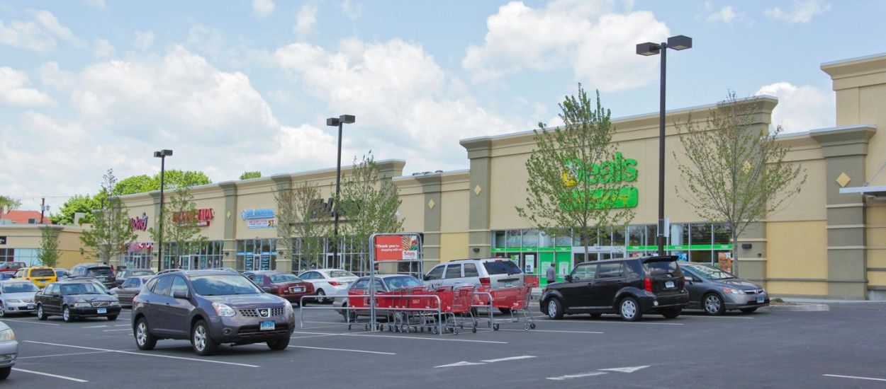 Shopping center parking lot with cars and carts in front of a storefront under a cloudy sky