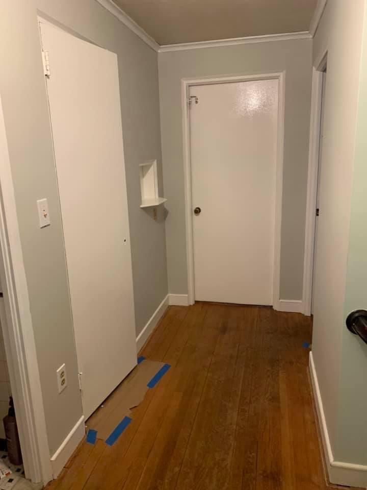 Narrow hallway with gray walls, white doors, wood floor, and blue painter’s tape on the floor