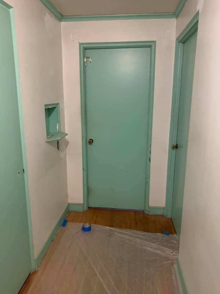 Narrow hallway with mint green doors and trim, white walls, and a plastic-covered floor during painting or renovation.