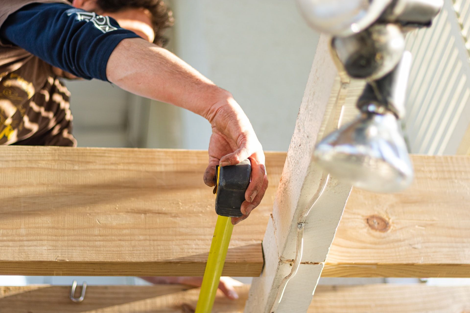 Person using a yellow tape measure on a wooden plank near a sink faucet