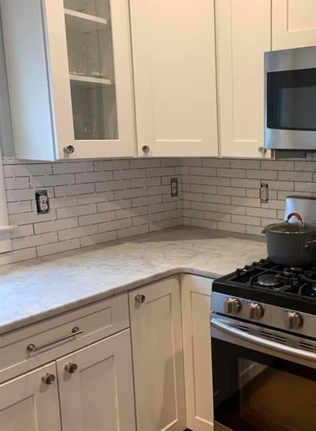 Bright white kitchen corner with subway tile backsplash, marble counters, cabinets, and a gas stove.