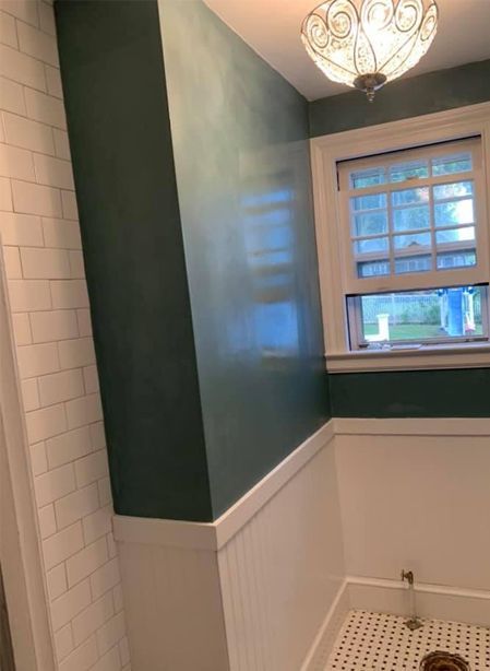 Small bathroom with dark green walls, white wainscoting, tiled shower, window, and ceiling light.