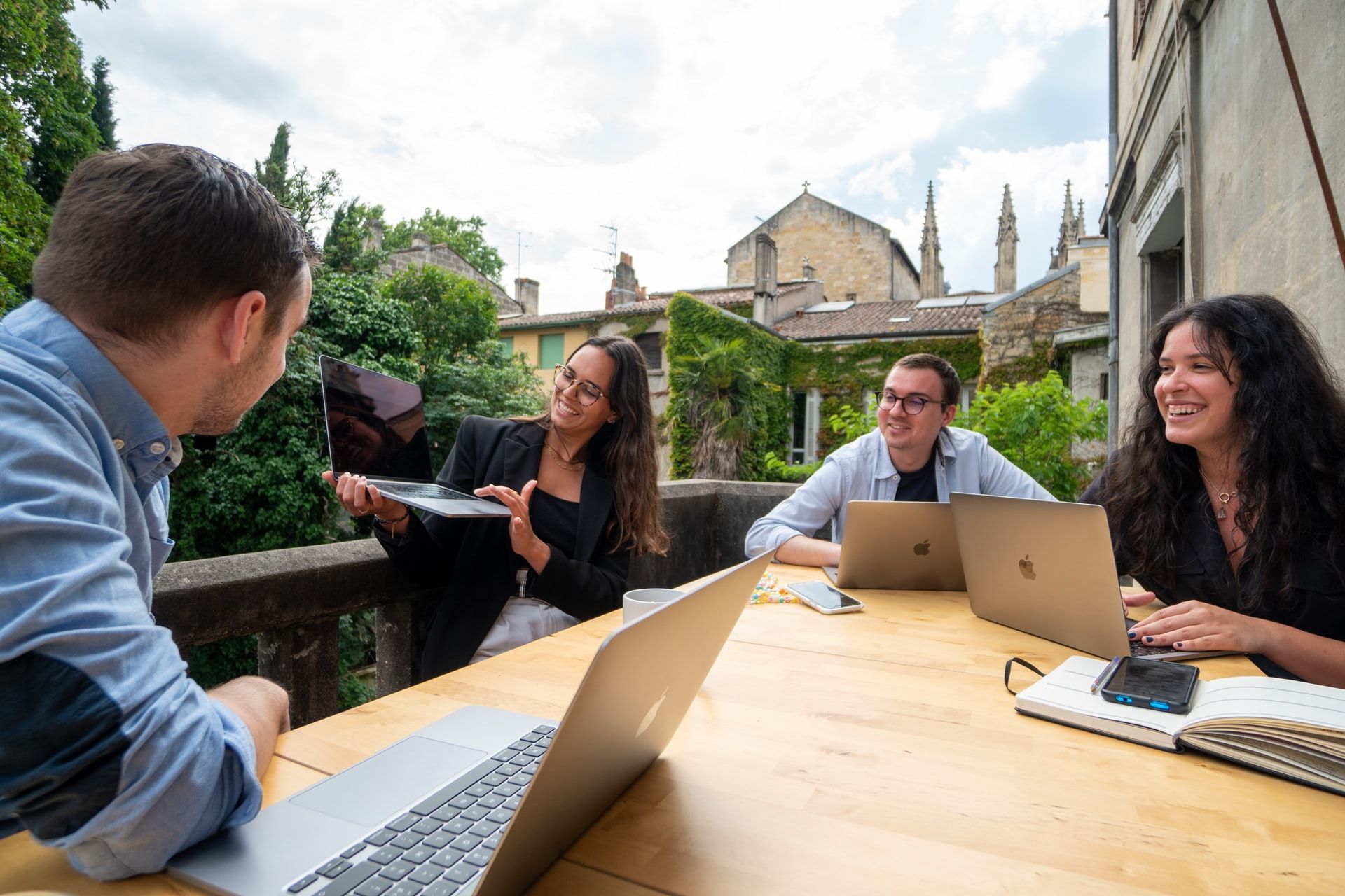 People meeting outdoors at a wooden table with laptops in a courtyard