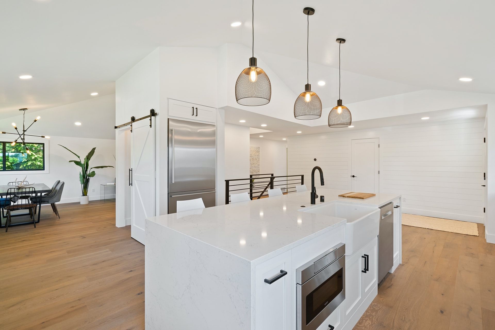 Bright modern kitchen with white island, pendant lights, wood floors, and open dining area