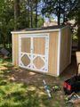 White and tan backyard shed with double barn doors and white trim among trees