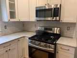 Modern white kitchen with stainless steel stove and microwave, marble backsplash, and light countertops