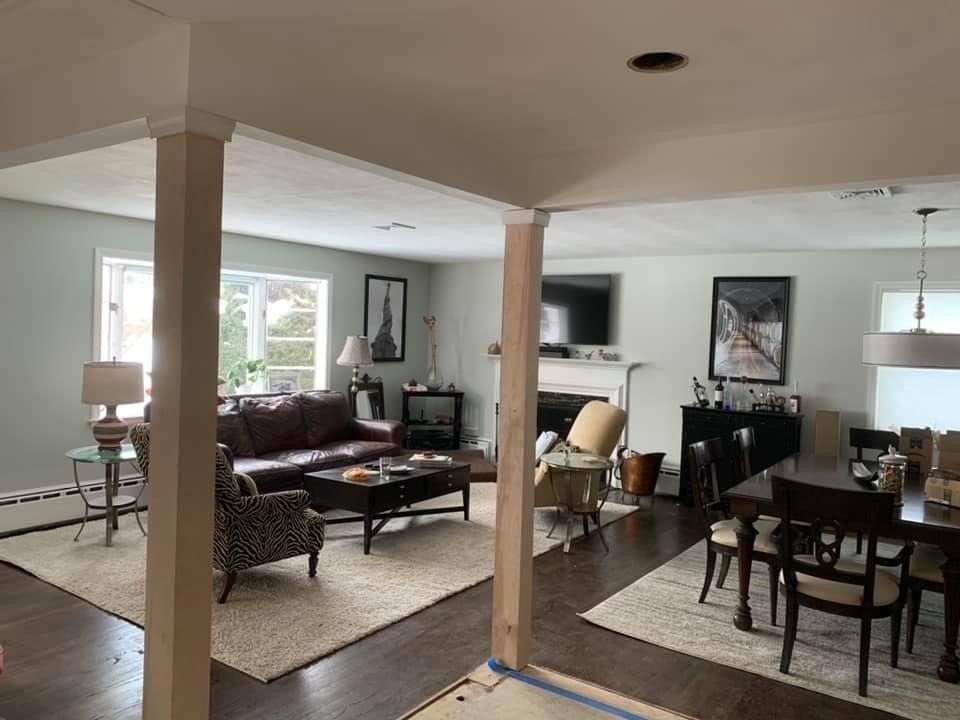 Open living and dining room with beige columns, dark furniture, and bright windows
