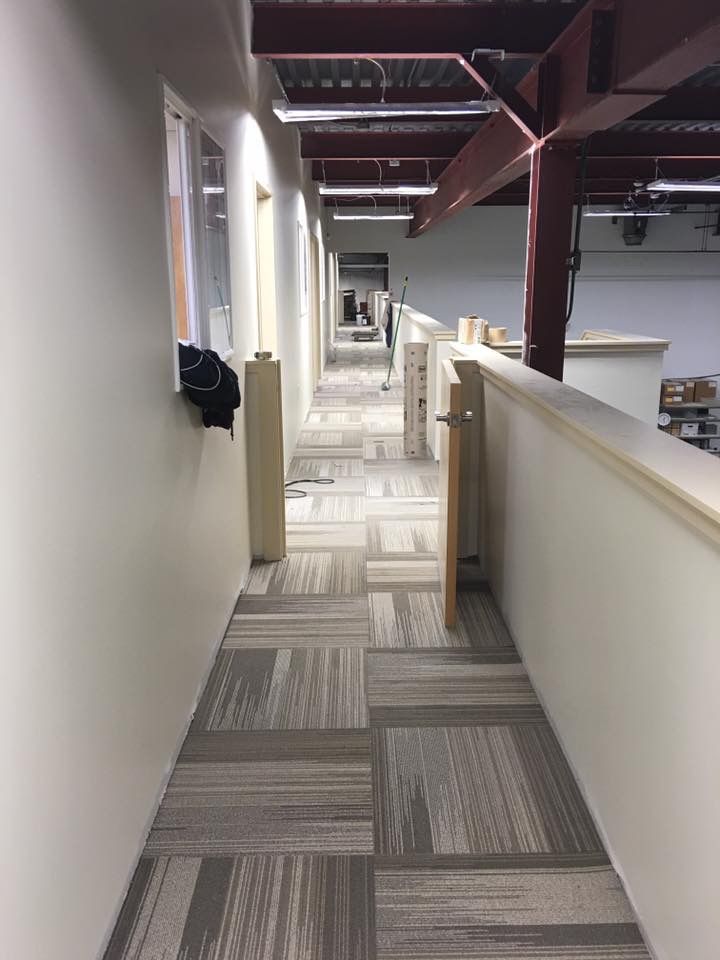 Office hallway with patterned carpet, white walls, and exposed ceiling beams, viewed from one end.