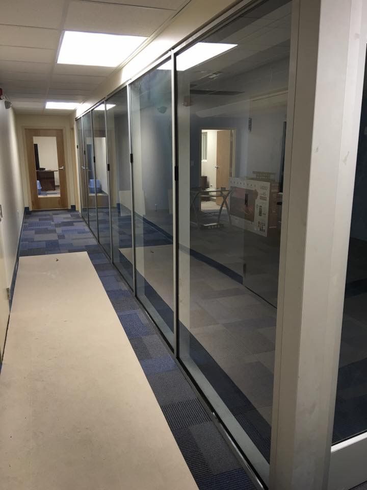 Office hallway with glass-walled rooms and blue carpet runner extending into the distance