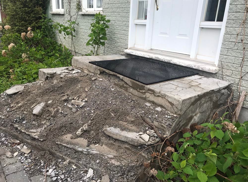 Un porche en béton avec un tapis noir dessus devant une maison.