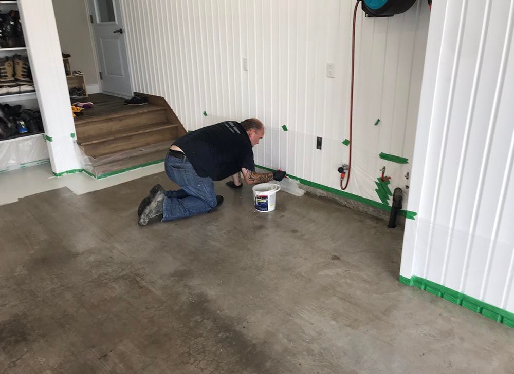 Un homme est à genoux dans un garage et peint le sol.