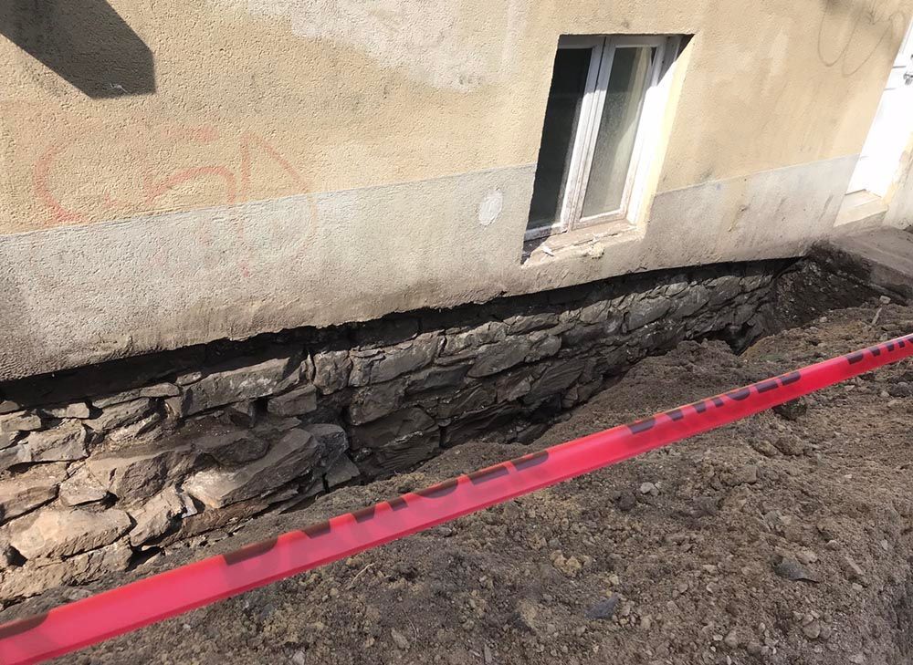 Un bâtiment avec un trou dans les fondations et un ruban rouge autour.