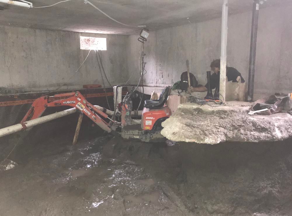 Un homme travaille dans un sous-sol avec une petite excavatrice.