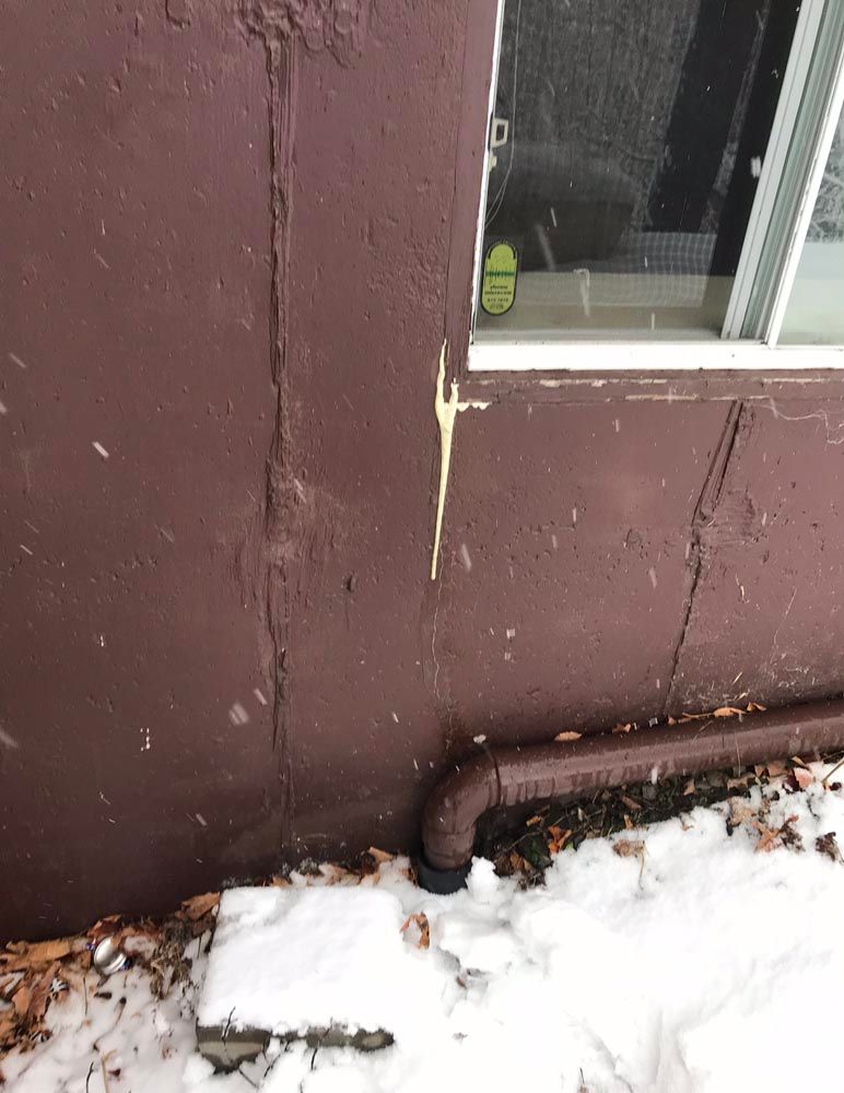 Un mur marron avec une fenêtre et un tuyau dans la neige.