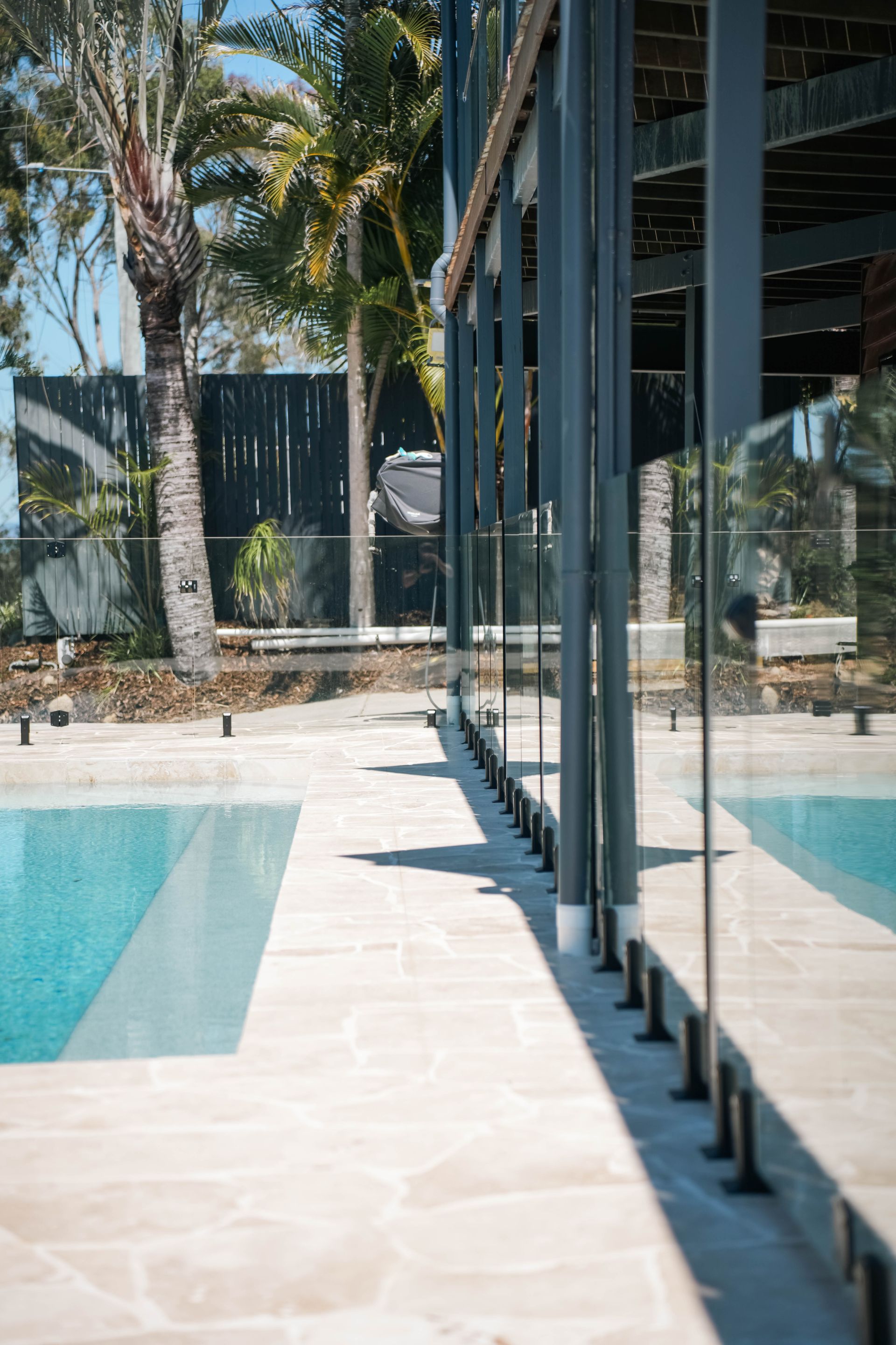 Pool With Blue Water, Surrounded By Glass Fence, Under A Cloudy Sky — Concrete Pool Projects in Gladstone Central, QLD