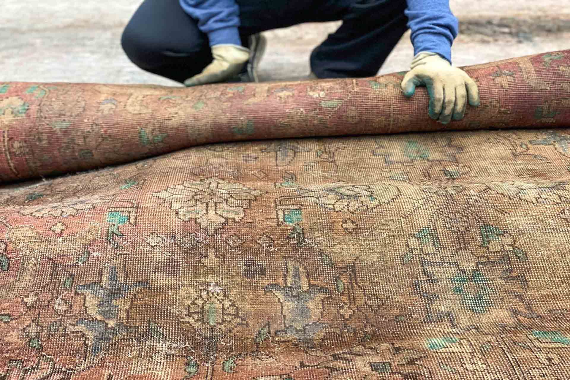 A man is kneeling down to roll a rug on the ground.