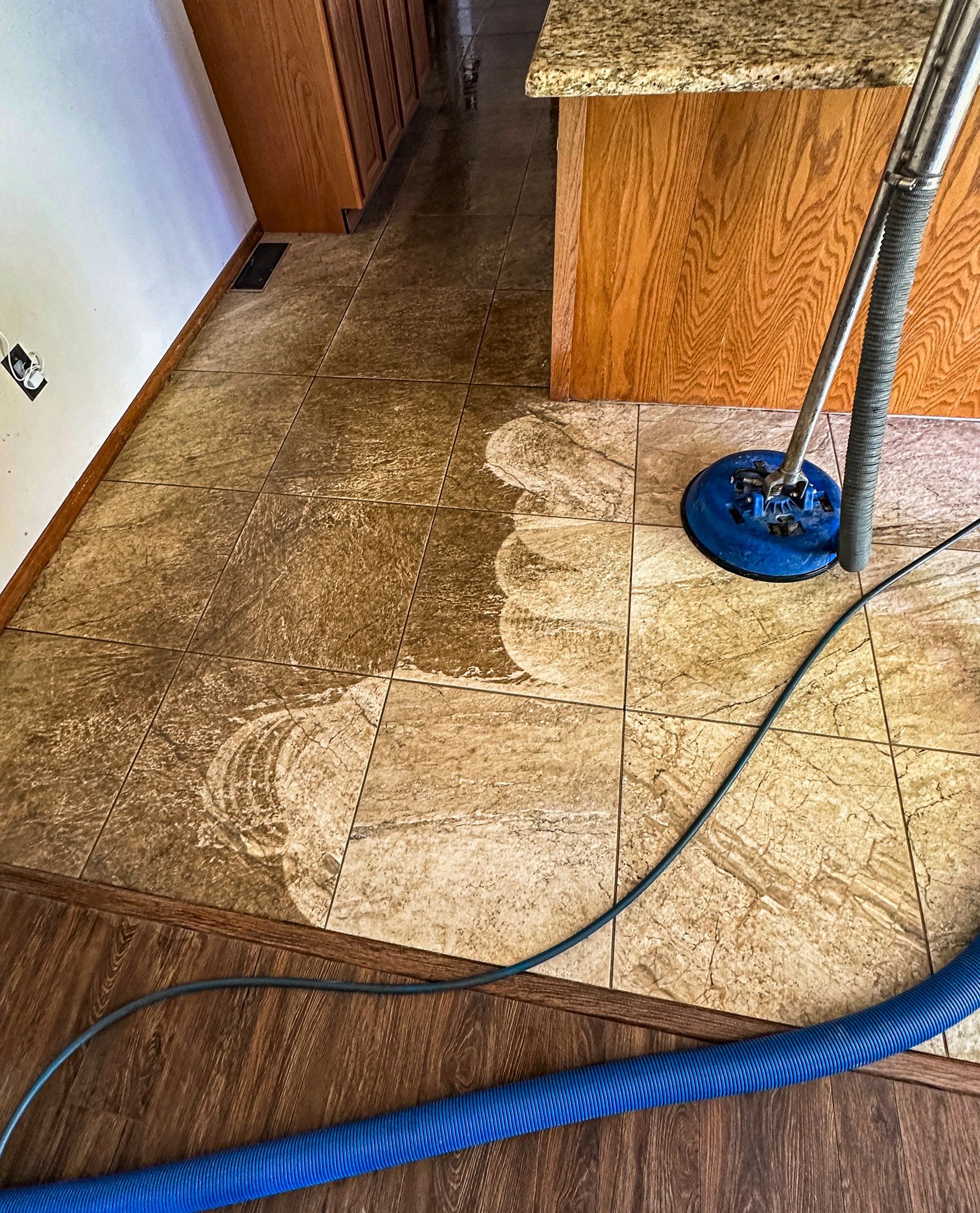 A vacuum cleaner is cleaning a tile floor in a kitchen.