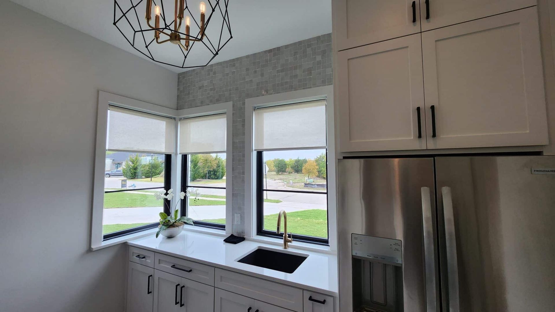 Kitchen corner with white cabinets, a black sink, and two windows with shades.