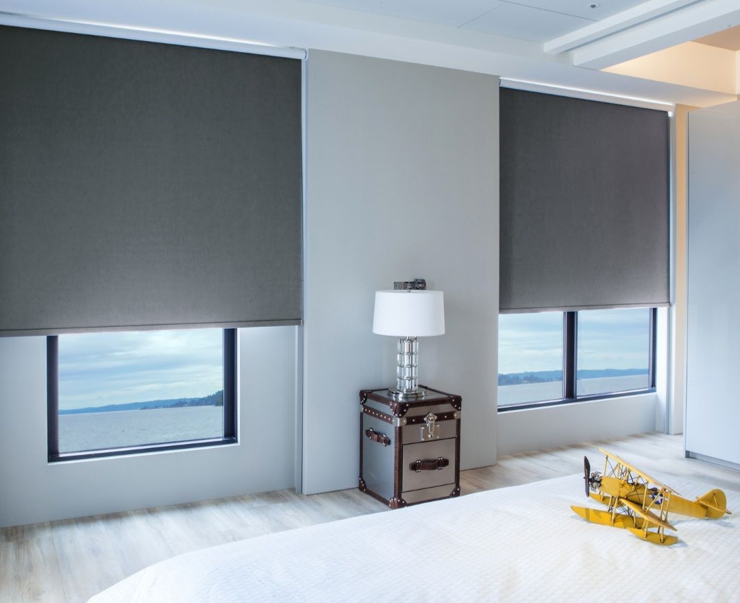 Bedroom with gray roller shades over windows, a nightstand, and a toy airplane.