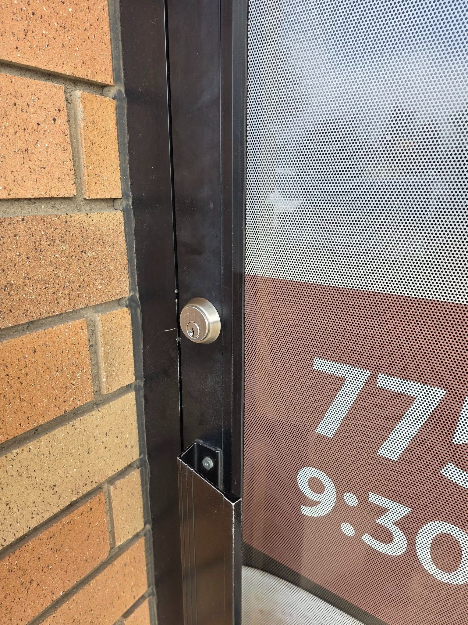 Close-up of a brick wall and black door frame beside a window with white numbers visible