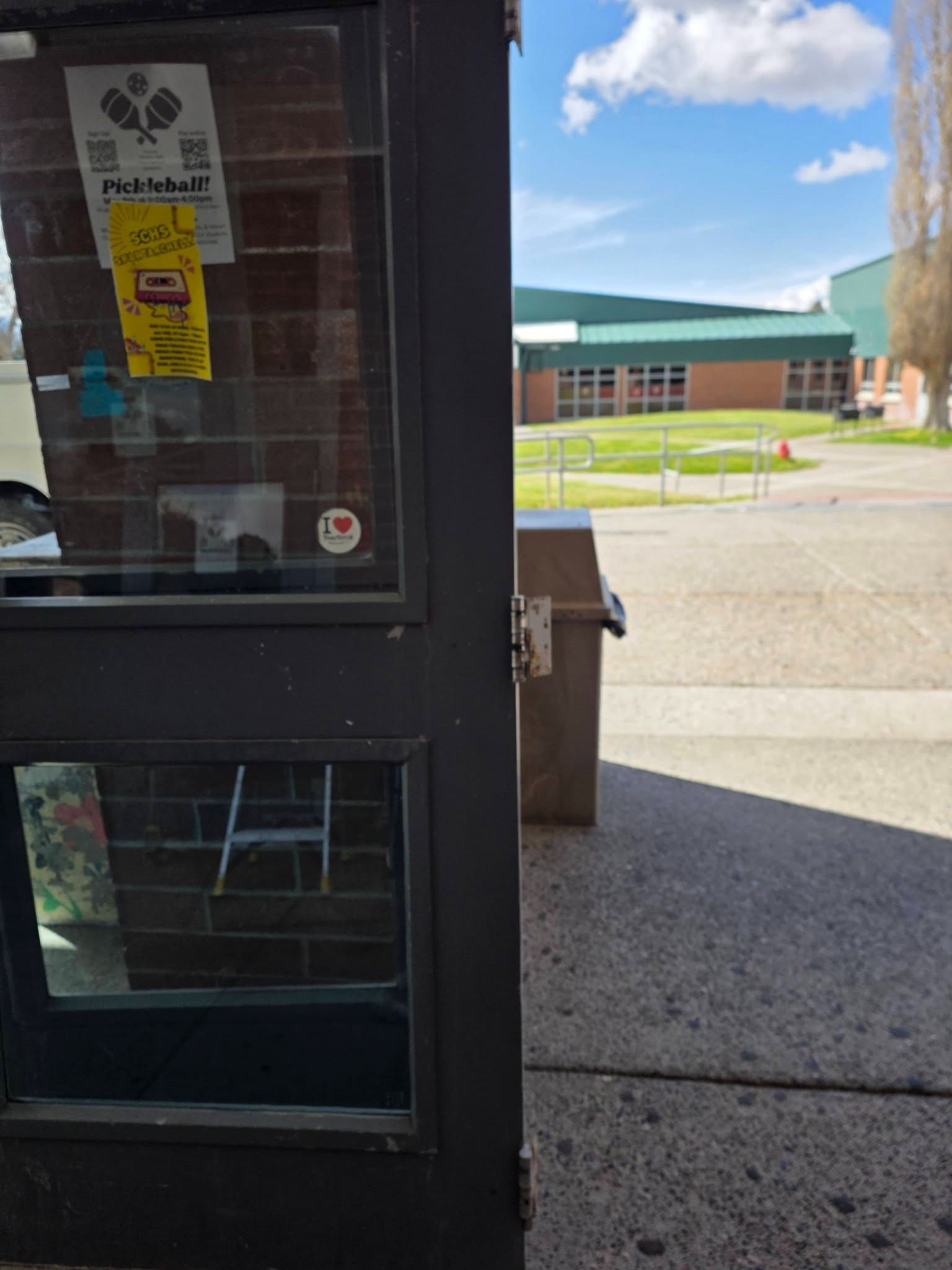 Open door to a school courtyard with brick building and blue sky outside.