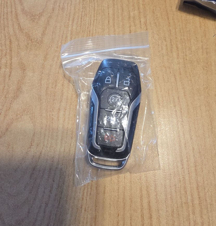 Car key fob in a clear plastic bag on a wooden table.