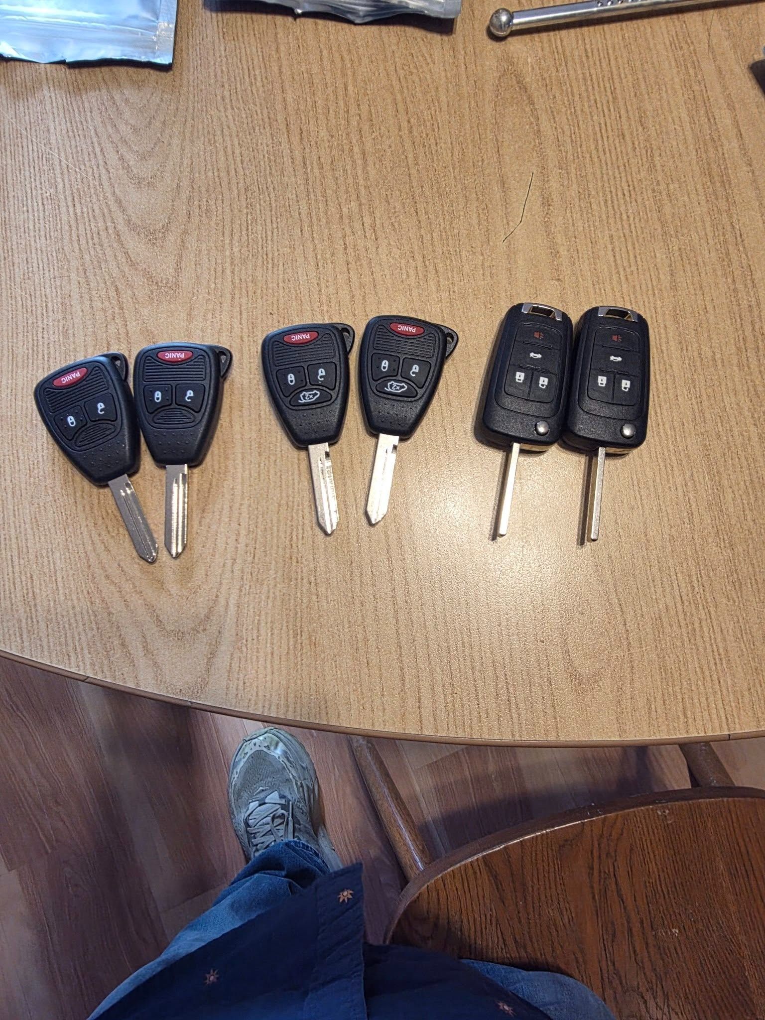 Six car key fobs arranged on a wooden table, with a blue shoe partially visible at the bottom.