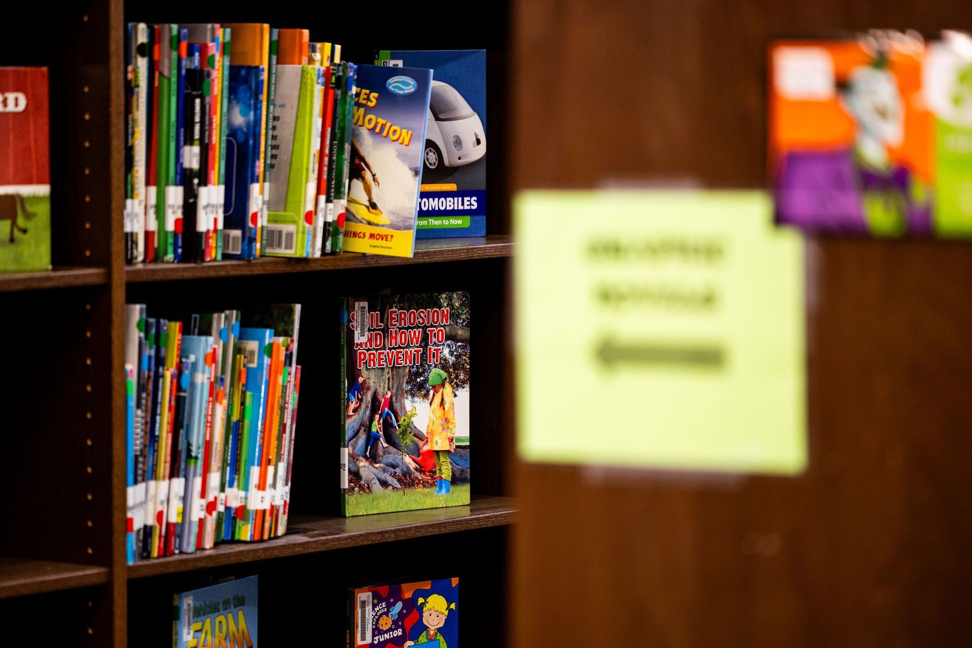 Bookshelves with colorful books in a library; a blurred green note is pinned on a wooden wall.