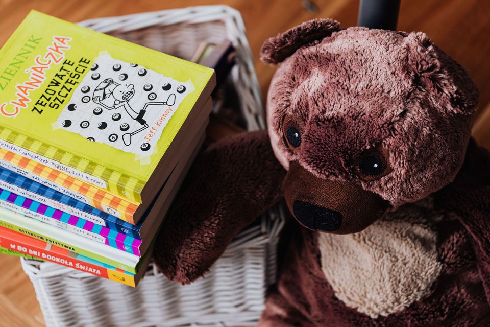 Brown teddy bear beside a stack of colorful books on a woven basket