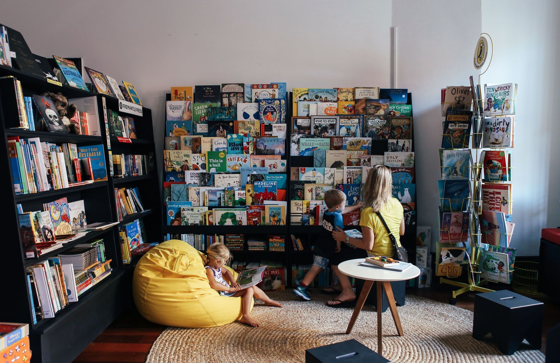 Bright playroom with shelves of toys, a yellow beanbag, and children sitting on the floor and sofa.