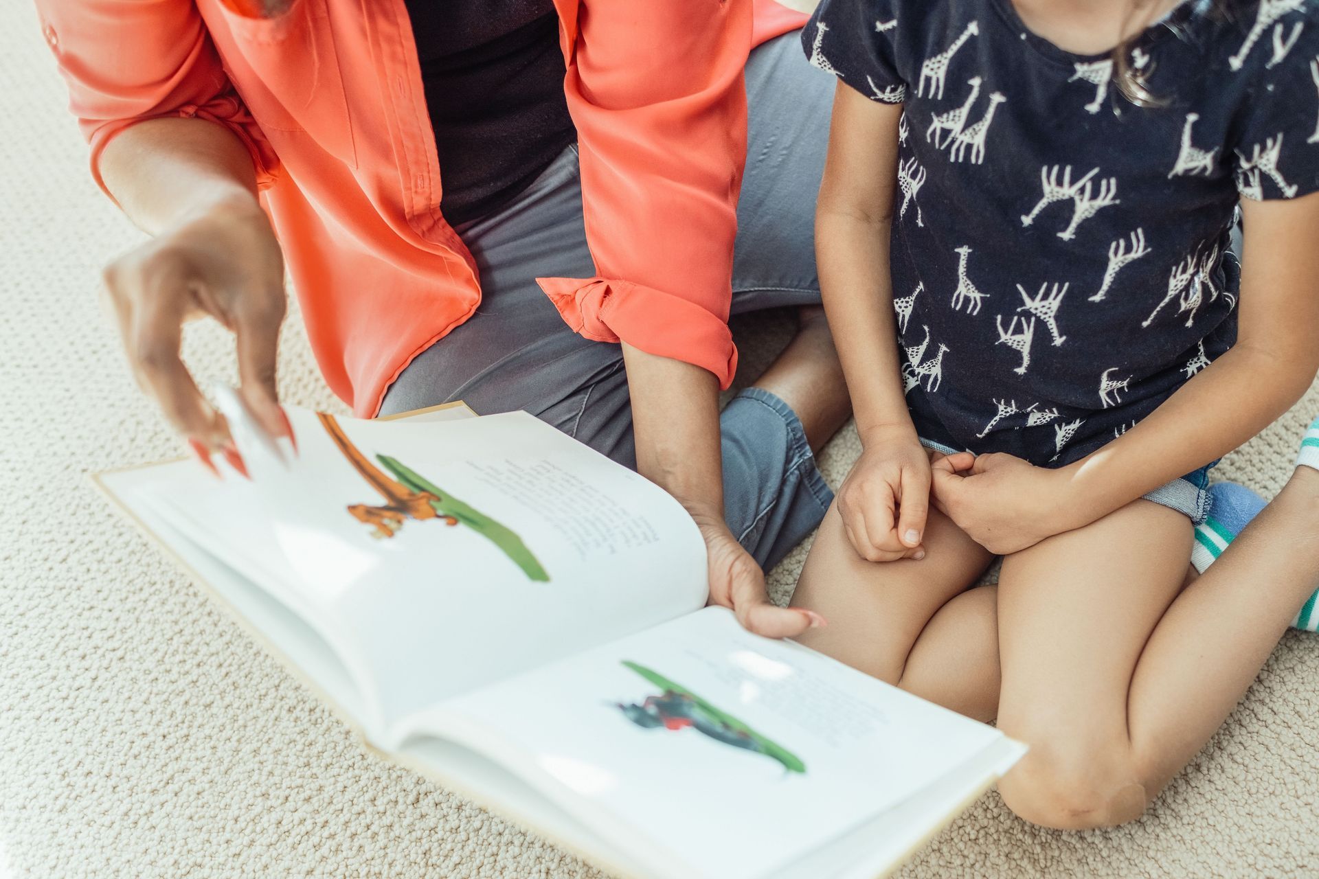 Adult and child reading a picture book together on the floor, with colorful illustrations visible