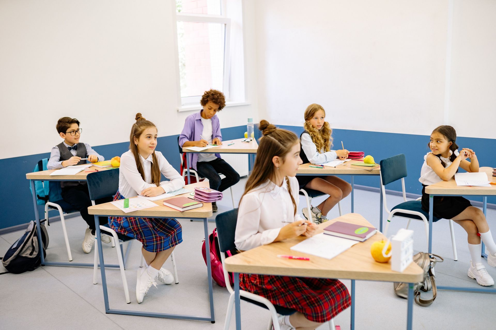 Students seated at desks in a bright classroom, writing and reading during class.