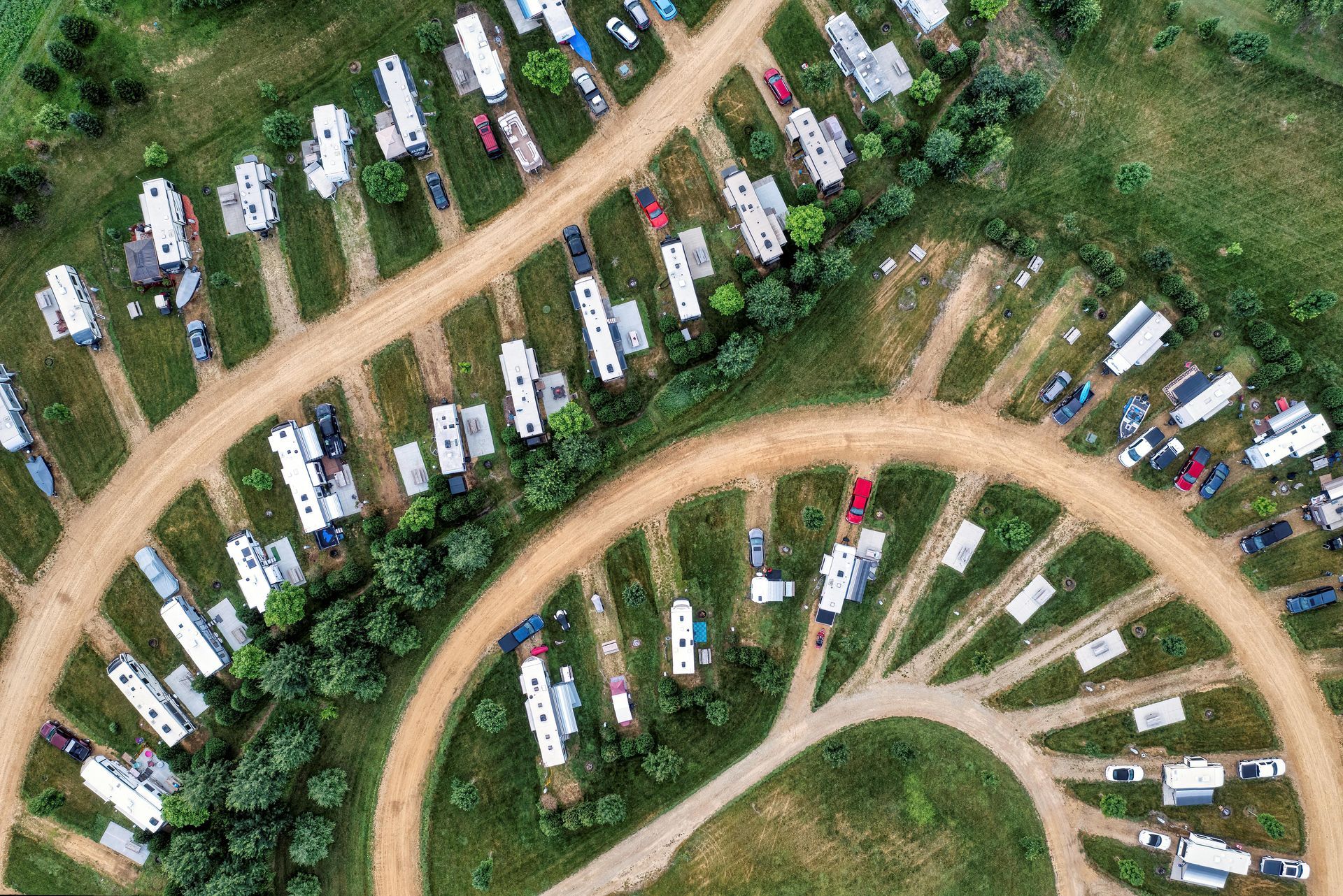 Aerial view of rows of RVs and trailers parked along curving dirt roads in a grassy campground